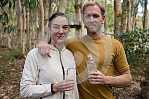 Hiker couple standing in the forest together holding water bottles