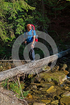 Hiker crosses mountain river by a makeshift bridge.