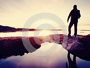 Hiker in dark sportswear with poles and sporty backpack. Coastline trail on rocky shore. Alone tourist enjoy