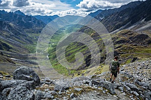 Hiker descending steep rocky trail above glacial valley in Alaska