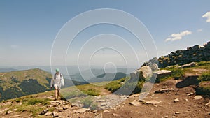 Hiker Enjoying Mountain Vista, Lone hiker walking on a mountain trail with a vast landscape in the background.