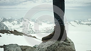 Hiker feet in leather boot stomps on rock at snowy mountain scenic view