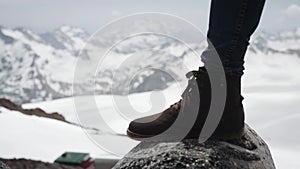 Hiker feet in leather boot stomps on stone at snowy mountain scenic view