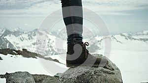 Hiker feet in leather shoe stomps on rock at snowy mountain scenic view