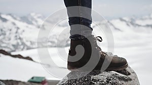 Hiker feet in leather shoe stomps on stone at snowy mountain scenic view