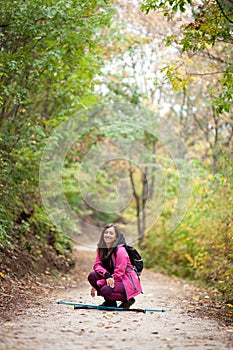 Hiker girl crouching on a trail in the mountains. Backpacker with pink jacket in a forest. Healthy fitness lifestyle outdoors