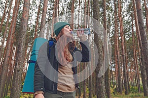 Hiker girl enjoying water. Happy woman tourist with backpack drinking water from bottle in nature.