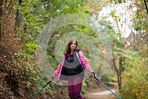 Hiker girl jumping on a trail in the mountains. Backpacker with hiking poles and pink jacket in a forest. Happy lifestyle outdoors