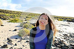 Hiker girl smiling at camera outdoors. Happy young traveler woman exploring Lanzarote hills and beaches in a sunny and windy day.