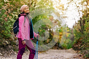 Hiker girl standing on a wide trail in the mountains. Backpacker with pink jacket in a forest. Healthy fitness lifestyle outdoors