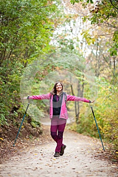 Hiker girl standing on a wide trail in the mountains. Backpacker with pink jacket in a forest. Healthy fitness lifestyle outdoors