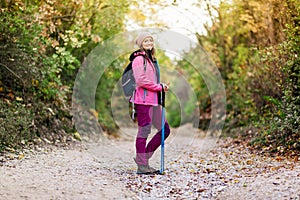 Hiker girl standing on a wide trail in the mountains. Backpacker with pink jacket in a forest. Healthy fitness lifestyle outdoors