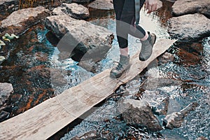 Hiker girl wades across the river on wooden Board, heavy Hiking boots