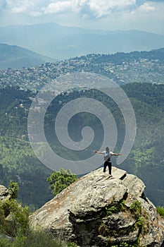 Hiker with his arms spread to the side standing on top of mountain ridge overlooking peaked mountains and forest valley against