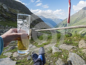 Hiker holding beer glass with foot in rubber clogs relaxing at view from Nurnberger Hutte hut, valley with mountain photo