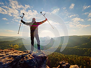 Hiker with hurts knee. Man with leg in join immobilizer stay on summit and raise medicine crutch