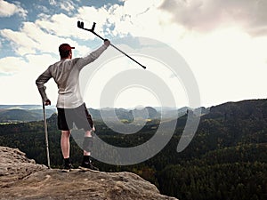 Hiker huts knee. Man with leg in join immobilizer stay on summit and raise medicine cruth above head.