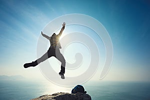 Hiker jumping on sunrise seaside cliff edge