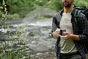 Hiker with a large hiking backpack standing on the bank of the river