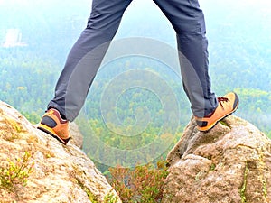 Hiker legs in comfortable trekking boots on rock. Man legs in light outdoor trousers, leather shoes