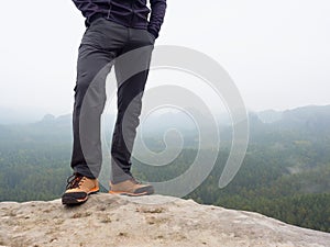 Hiker legs in comfortable trekking boots on rock. Man legs in light outdoor trousers, leather shoes