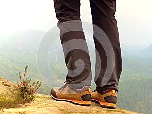 Hiker legs in comfortable trekking boots on rock. Man legs in light outdoor trousers, leather shoes