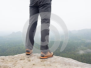 Hiker legs in comfortable trekking boots on rock. Man legs in light outdoor trousers, leather shoes