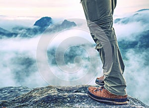 Hiker legs in trousers and leather trekking boots on summit