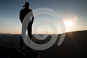 Hiker in long cap on rock empire and watching to Sun. Beautiful moment the miracle of nature