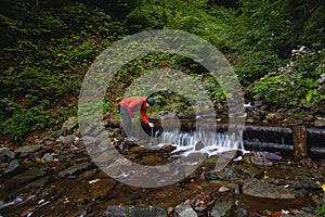 Hiker on a long trail refills drinking water from a mountain spring into a glass container. Replenishing clean water for cooking