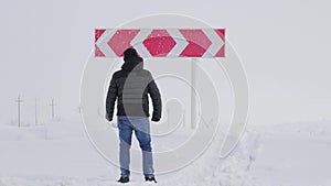 Hiker man with backpack choose in a road fork between two different path directions at the winter on road. Concept of