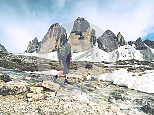 Hiker man with backpack crossing stream on stones in Dolomiti