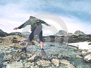 Hiker man with backpack crossing stream on stones in Dolomiti