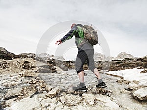 Hiker man with backpack crossing stream on stones in Dolomiti
