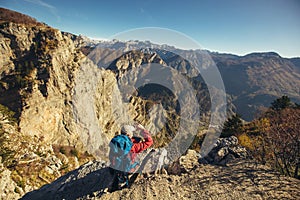 Hiker man with backpack standing on edge of cliff and looking at the mountains