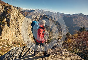 Hiker man with backpack standing on edge of cliff and looking at the mountains