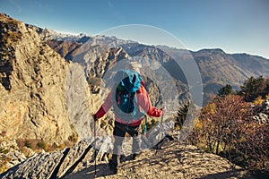 Hiker man with backpack standing on edge of cliff and looking at the mountains