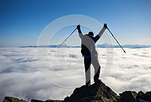 Hiker man on rocky hill on foggy valley with white clouds, snowy mountains and blue sky background.