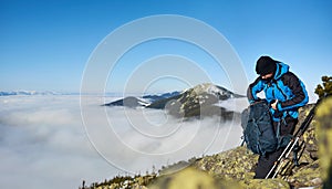 Hiker man on rocky hill on foggy valley with white clouds, snowy mountains and blue sky background.