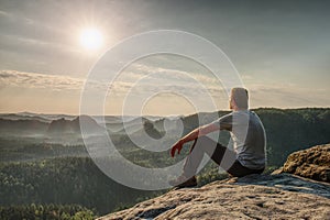 Hiker man in sportswear sitting on cliff edge