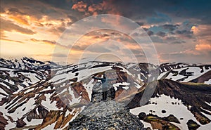 Hiker man standing with arms raised on the cliff with volcanic mountain and snow covered from Blanhjukur trail on summer in the