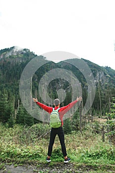 Hiker man stands with arms raised against the backdrop of the nature`s pristine nature and enjoys freedom. Vertical photo of man