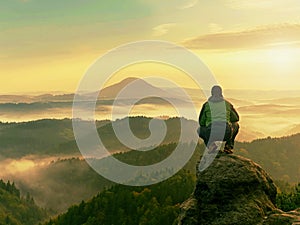 Hiker man take a rest on mountain peak. Man sit on sharp summit and enjoy spectacular view.