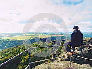 Hiker man take a rest on mountain peak. Man sit on summit view point, bellow cloudy valley