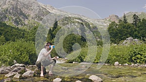 Hiker man taking bottle of water from mountain stream at summer travel