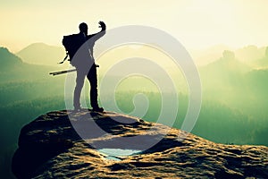 Hiker on peak. Backpacker with poles in hand shadowing eyes, spring daybreak