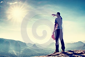 Hiker on peak of rock shadowing eyes and watching over the mist