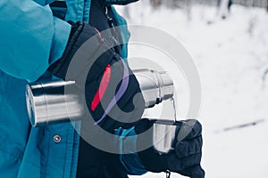 Hiker pours tea from the thermos in the winter forest