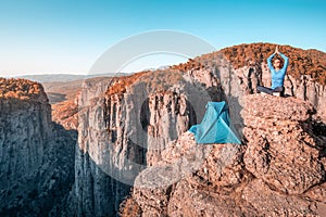 Hiker practices yoga and meditation next to her tent against the backdrop of a deep mountain gorge. Zen and fitness in