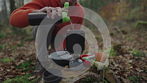 Hiker prepares food and pours water from bottle into pot. Traveler in forest cooks food with small cooking stove. Man